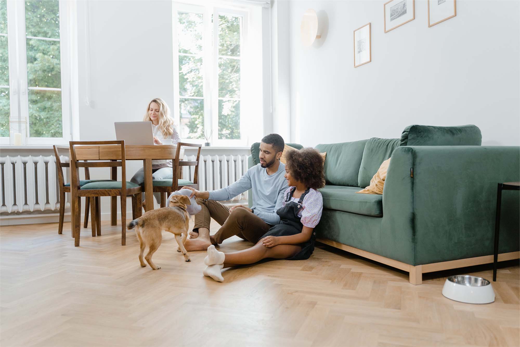 Une famille à la maison : un père et sa fille jouent avec leur chien pendant que la mère travaille à la table