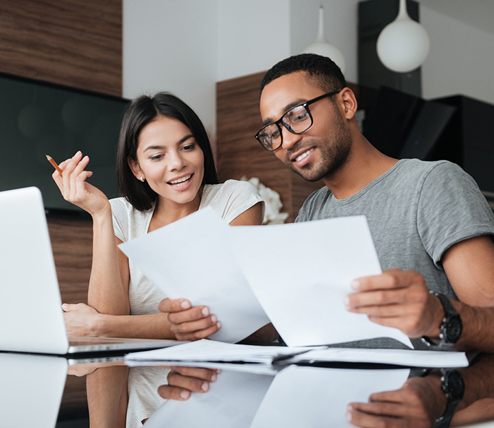 Un couple souriant qui lit des documents ensemble à une table, à côté d'un ordinateur portable